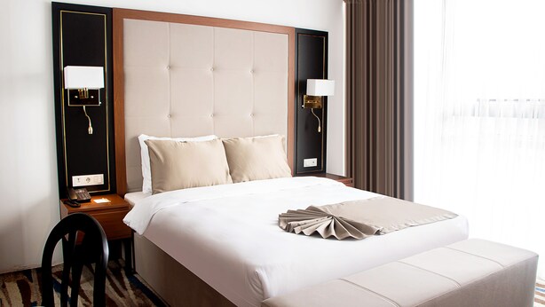 A hotel room with a large bed, a bedside table with a lamp, a chair, and a view of the outdoors through the window. - Shelter Inn Hotel & Spa (Ankara)