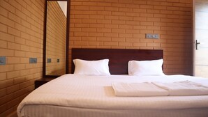 Ein Hotelzimmer mit Ziegelwand, Holzkopfteil, zwei weißen Kissen, einem ordentlich bezogenen Bett mit weißem Frotteehandtuch und einem Spiegel, der den Raum widerspiegelt.