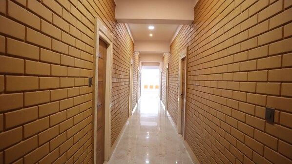 A corridor with brick walls and a shiny floor, leading to a bright room with orange chairs.