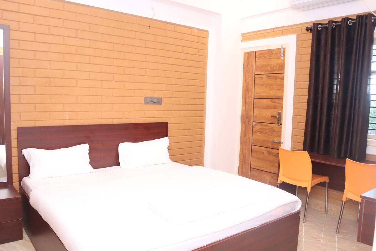 Une chambre d’hôtel avec un lit doté d’une tête de lit en bois, un bureau avec une chaise et une fenêtre avec des rideaux.