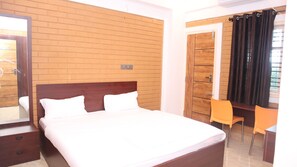 A hotel room with a wooden headboard bed, a desk with a chair, and a window with curtains.