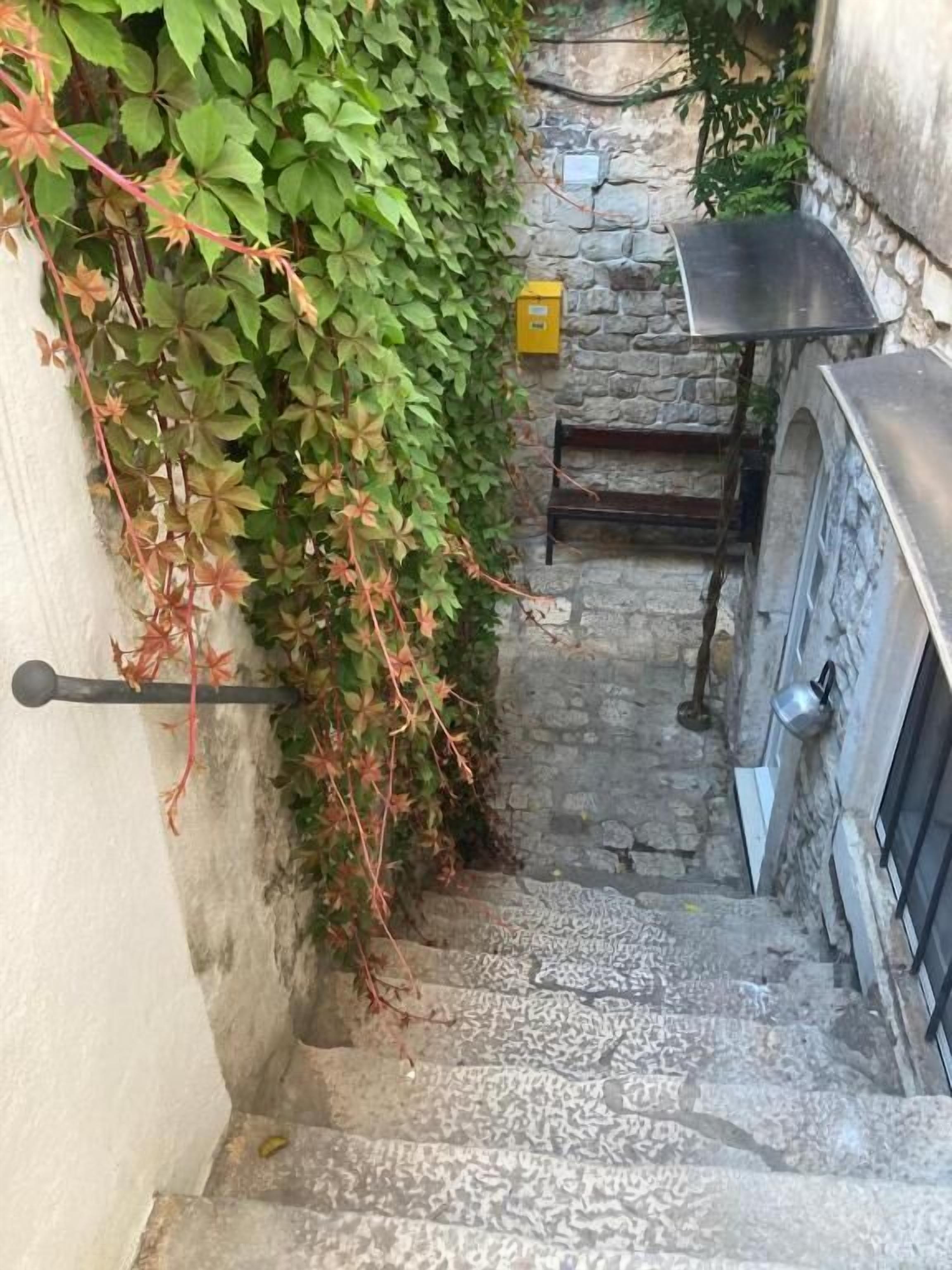 Eine enge Steintreppe führt zu einer Steinmauer mit einem Metallgitter und einem kleinen Tisch.