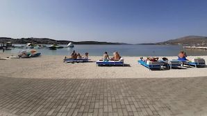 Ein Strand mit Liegestühlen und Sonnenschirmen, einem klaren Himmel und Booten im Wasser.