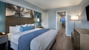 Ein Hotelzimmer mit einem großen Bett, einem Nachttisch mit Telefon, einer Schreibtischlampe und einem an der Wand befestigten Fernseher.