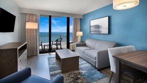 Ein Hotelzimmer mit Balkon, einer Couch, einem Couchtisch, einem Fernseher und einem Gemälde.
