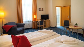 A hotel room with two beds, a desk, a chair, a television, and a small table with a plant. - Bischofshof Braustuben (Regensburg)
