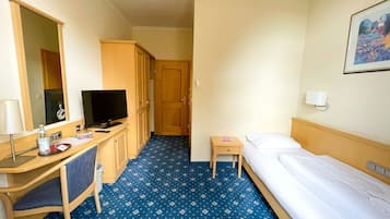 A hotel room with a desk, a bed, a TV, and a small table.