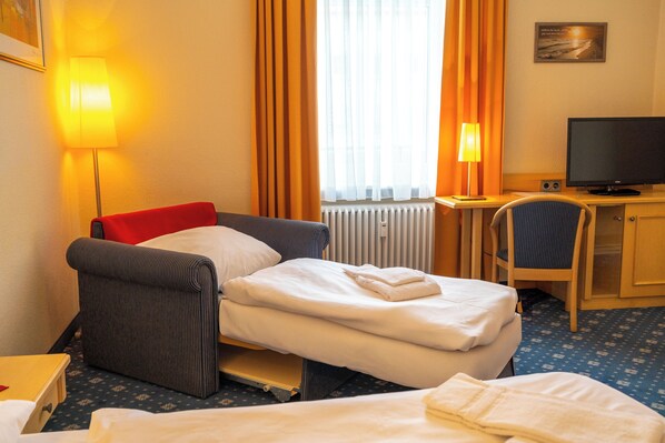A hotel room with a bed, a desk with a computer, a chair, and a window with curtains.