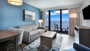 Ein modernes Hotelzimmer mit Balkon, einer Couch, einem Esstisch und einem Fernseher.