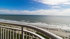 Blick auf einen Strand von einem Balkon mit Geländer, Meer und Strandbesuchern.