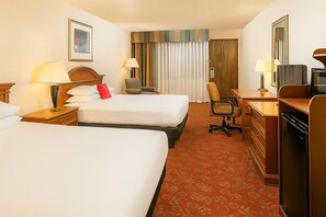 A hotel room with two beds, a desk, a chair, a dresser, and a large window with curtains.