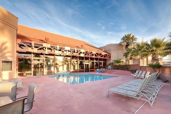 A hotel with a swimming pool, lounge chairs, and palm trees.