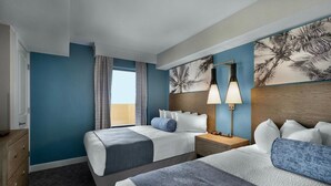 Ein Hotelzimmer mit zwei Betten, einem Holzkopfende, einem Nachttisch und einem Fenster mit Vorhängen.