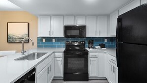Uma cozinha moderna com armários brancos, uma geladeira preta, micro-ondas e máquina de lavar louça.