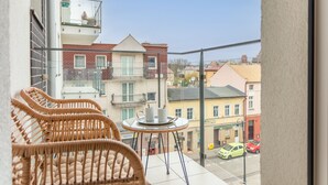 En balkon med fletstole og et lille bord, med udsigt over en gade med bygninger og biler.