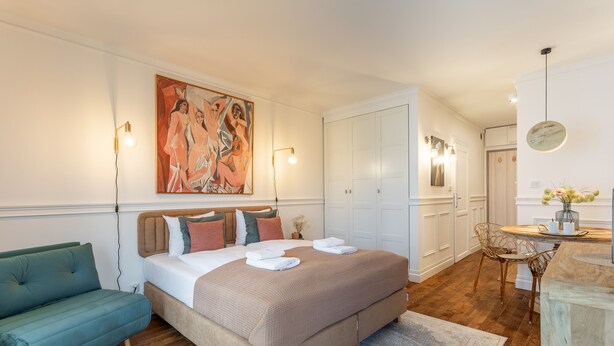 Et soveværelse med en stor seng, en grøn sofa, et billede på væggen og et spiseområde med et bord og stole.