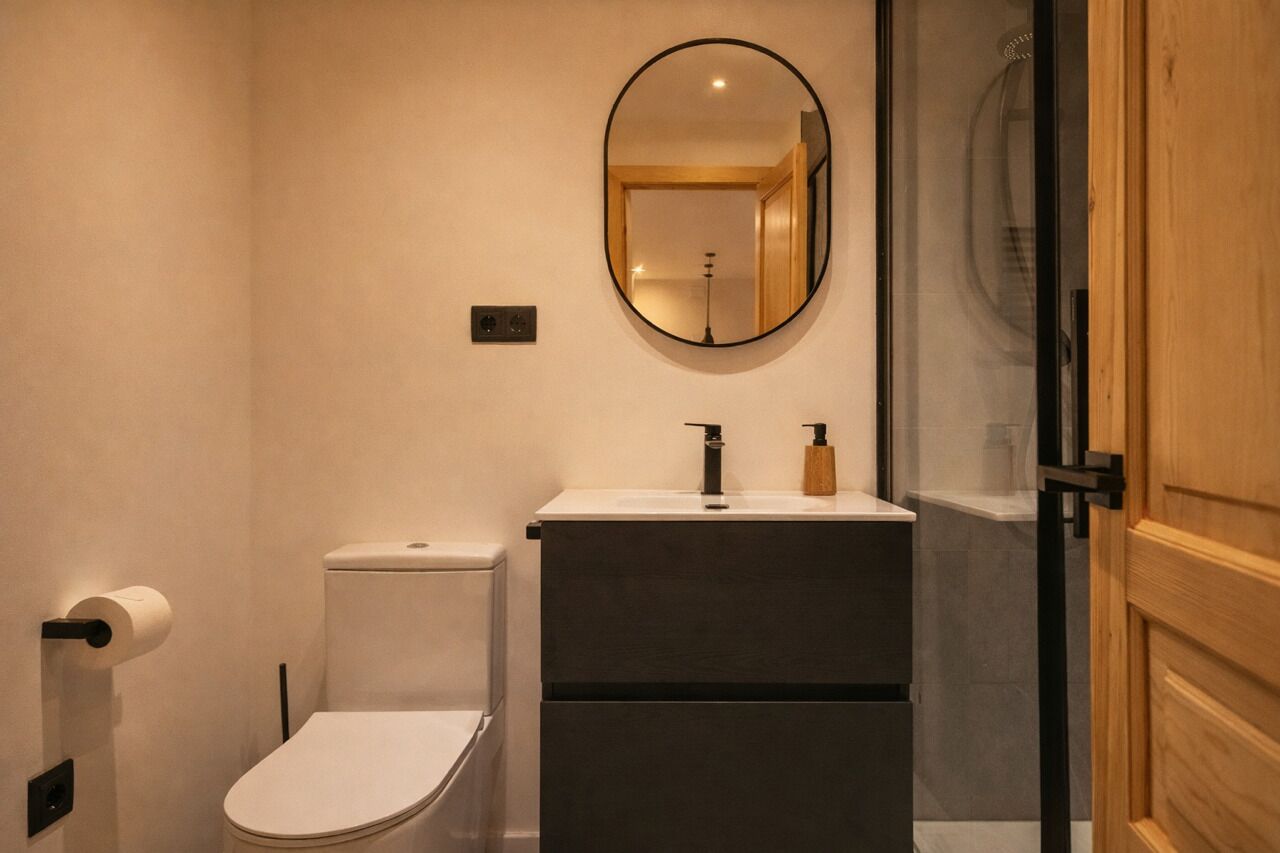 A modern bathroom with a toilet, a sink with a mirror, and a shower area.