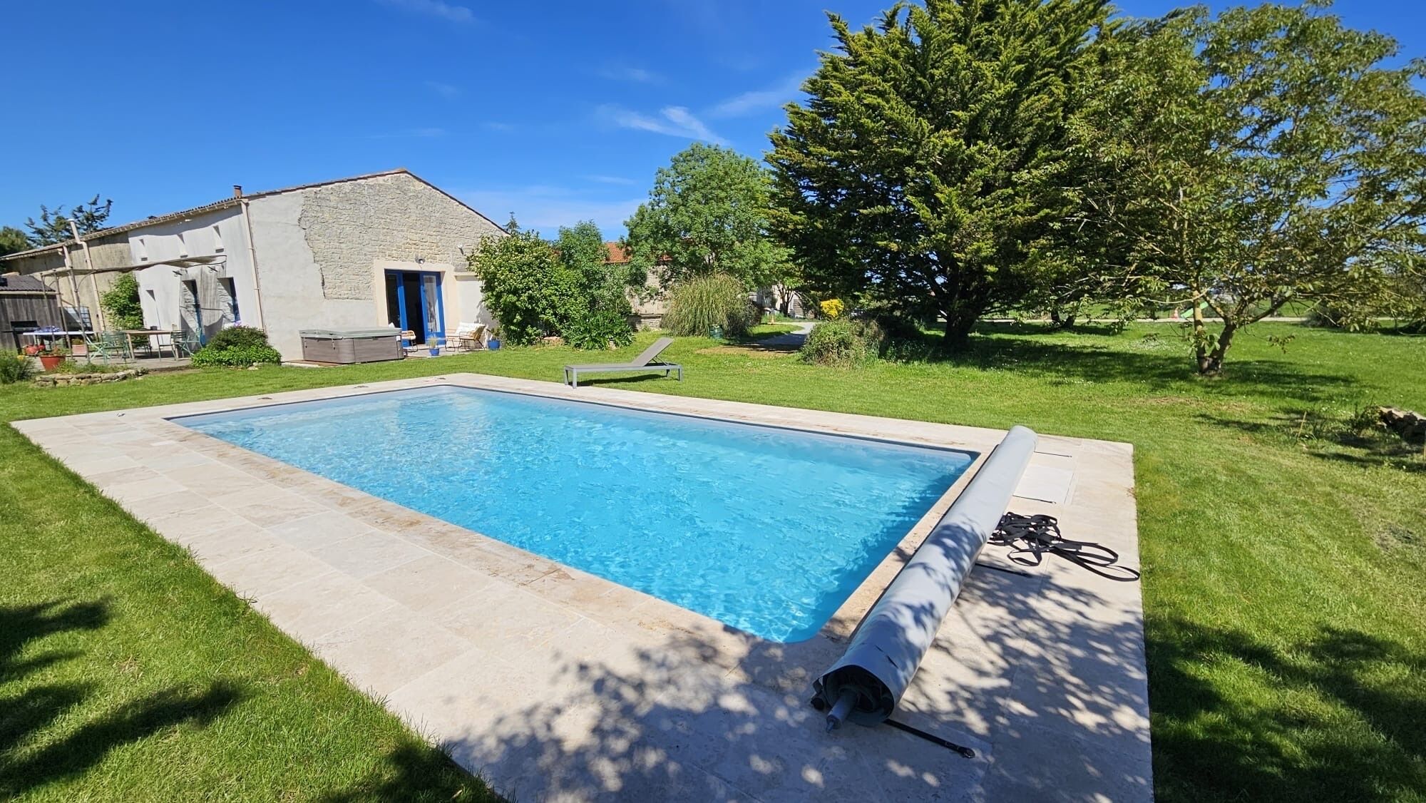 A rectangular swimming pool with a clear blue water surface, surrounded by a paved deck and a grassy lawn.