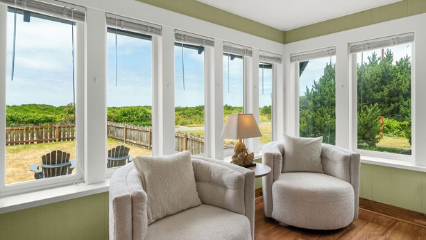 Una habitación con amplios ventanales, dos sillones, una mesita con lámpara y vistas a un área exterior cercada.