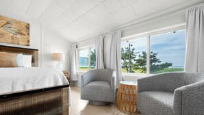 Un dormitorio con una cama, dos sillones, una mesa redonda, una lámpara y un ventanal con vistas.