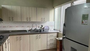 Una cocina con armarios de madera clara, un refrigerador de acero inoxidable y un ventanal que proporciona luz natural.