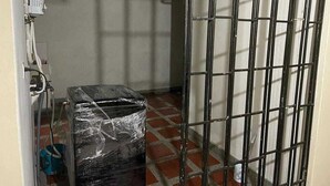 Una habitación con una puerta con barrotes, un pequeño calentador y suelo de baldosas.