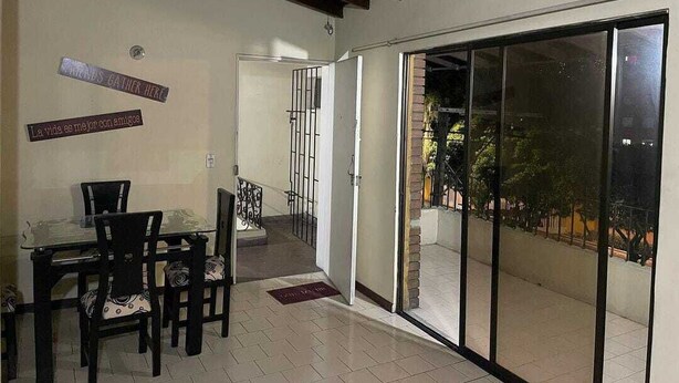 Un comedor con una mesa y sillas de vidrio, una puerta corrediza de vidrio que da a un balcón y un cartel en la pared.
