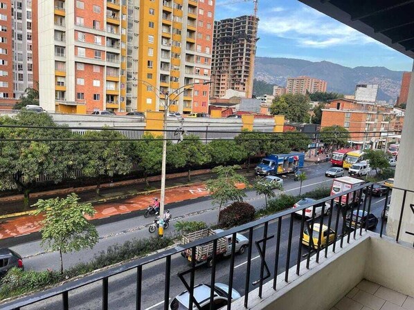 A view from a balcony overlooking a busy street with multiple vehicles, including cars, motorcycles, and trucks. There are tall buildings in the background, some under construction. - Friends Gather Hostal (Medellín)
