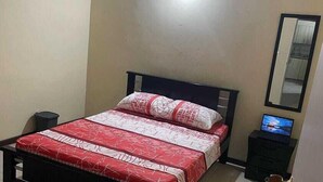 Un dormitorio con cama, mesita de noche, televisor y espejo.