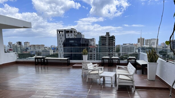 Una terraza en la azotea con suelo de baldosas, muebles de exterior blancos y vistas al horizonte de la ciudad.