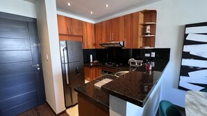 Una cocina moderna con armarios de madera, un refrigerador de acero inoxidable, una encimera negra y un horno empotrado.