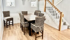 Uma área de refeições com mesa de madeira e cadeiras de fibra, escada com corrimão branco e decoração nas paredes.