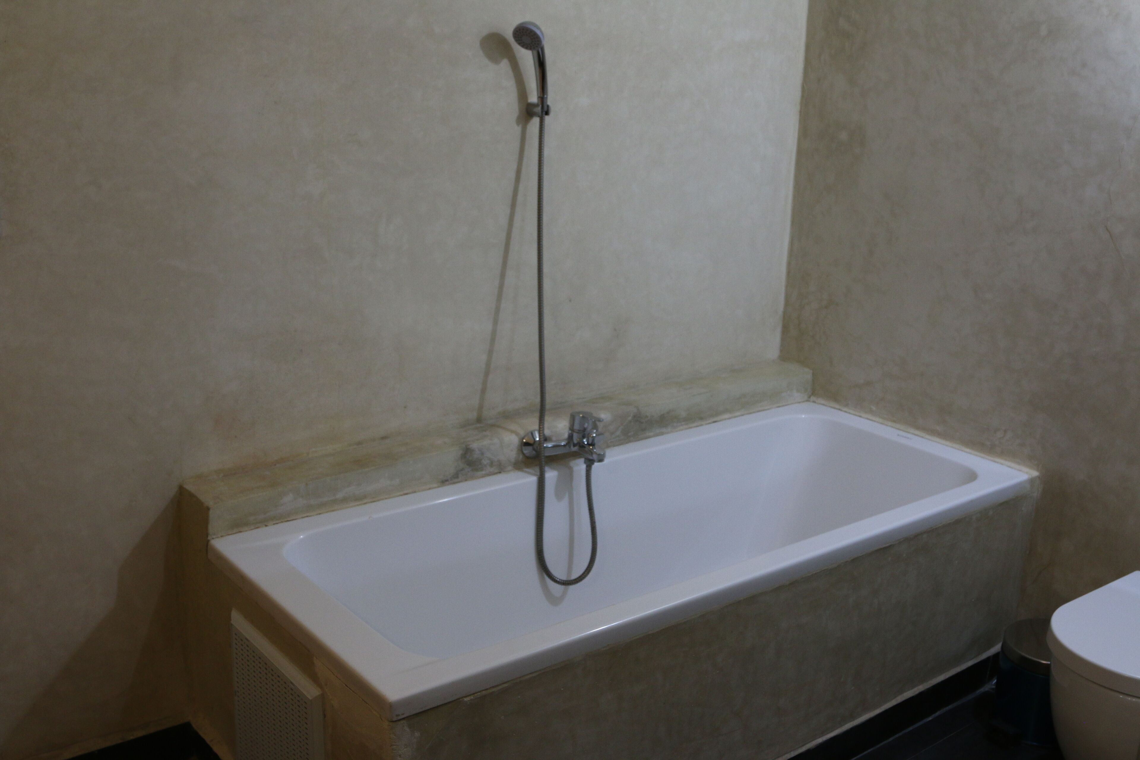 A bathroom with a white bathtub, a showerhead, and a toilet.