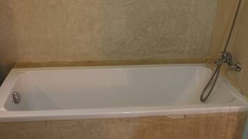 A standard rectangular bathtub with a shower head and faucet, set against a textured beige wall.