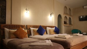 Une chambre d’hôtel avec deux lits, chacun doté d’une tête de lit en bois, de plusieurs oreillers et d’un téléviseur à écran plat fixé au mur.