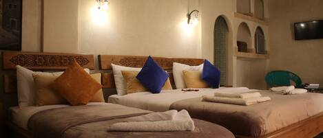 Habitación de hotel con dos camas, cada una con cabecero de madera, varios almohadones y un televisor de pantalla plana montado en la pared.
