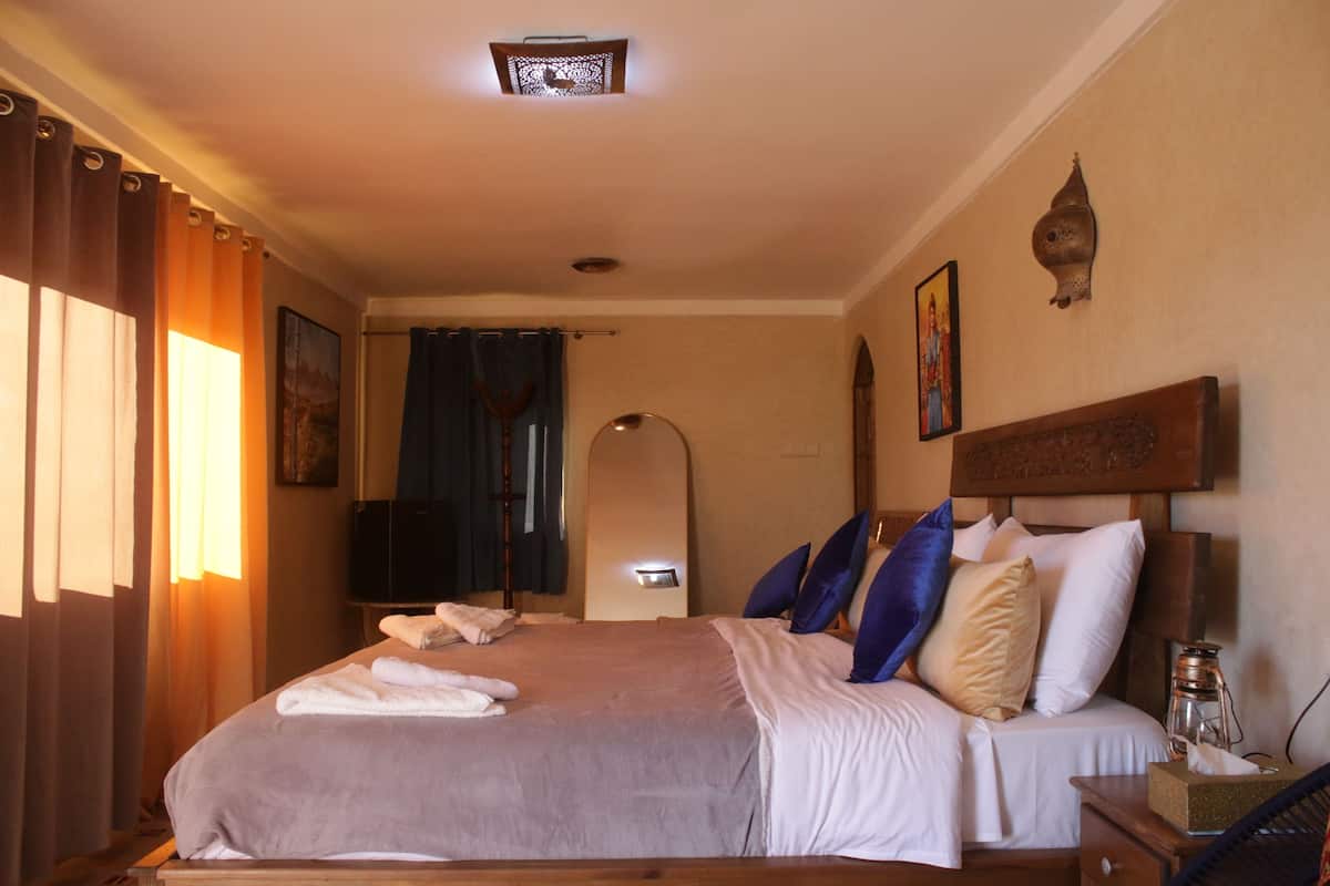 Een hotelkamer met een groot bed, een nachtkastje, een lamp en een raam met gordijnen.