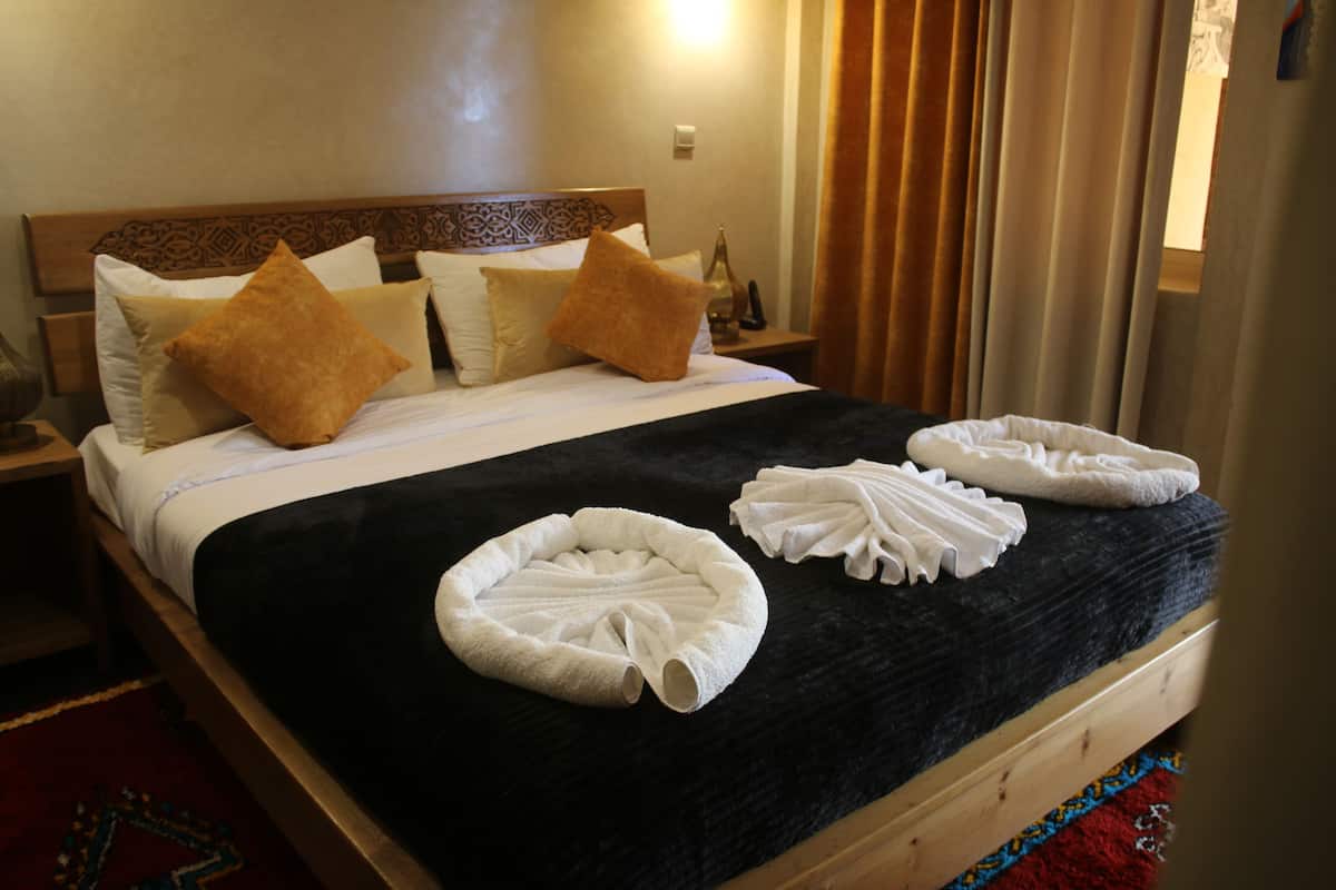 Een net opgemaakt bed met een zwart dekbed, witte kussens en een bruin sierkussen. Er liggen twee witte handdoeken op het bed gevouwen.