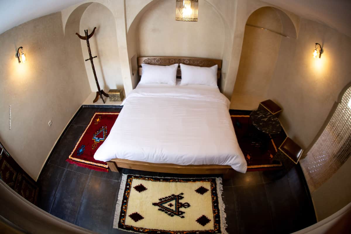 Een kamer met een bed, een vloerkleed en een wandlamp.