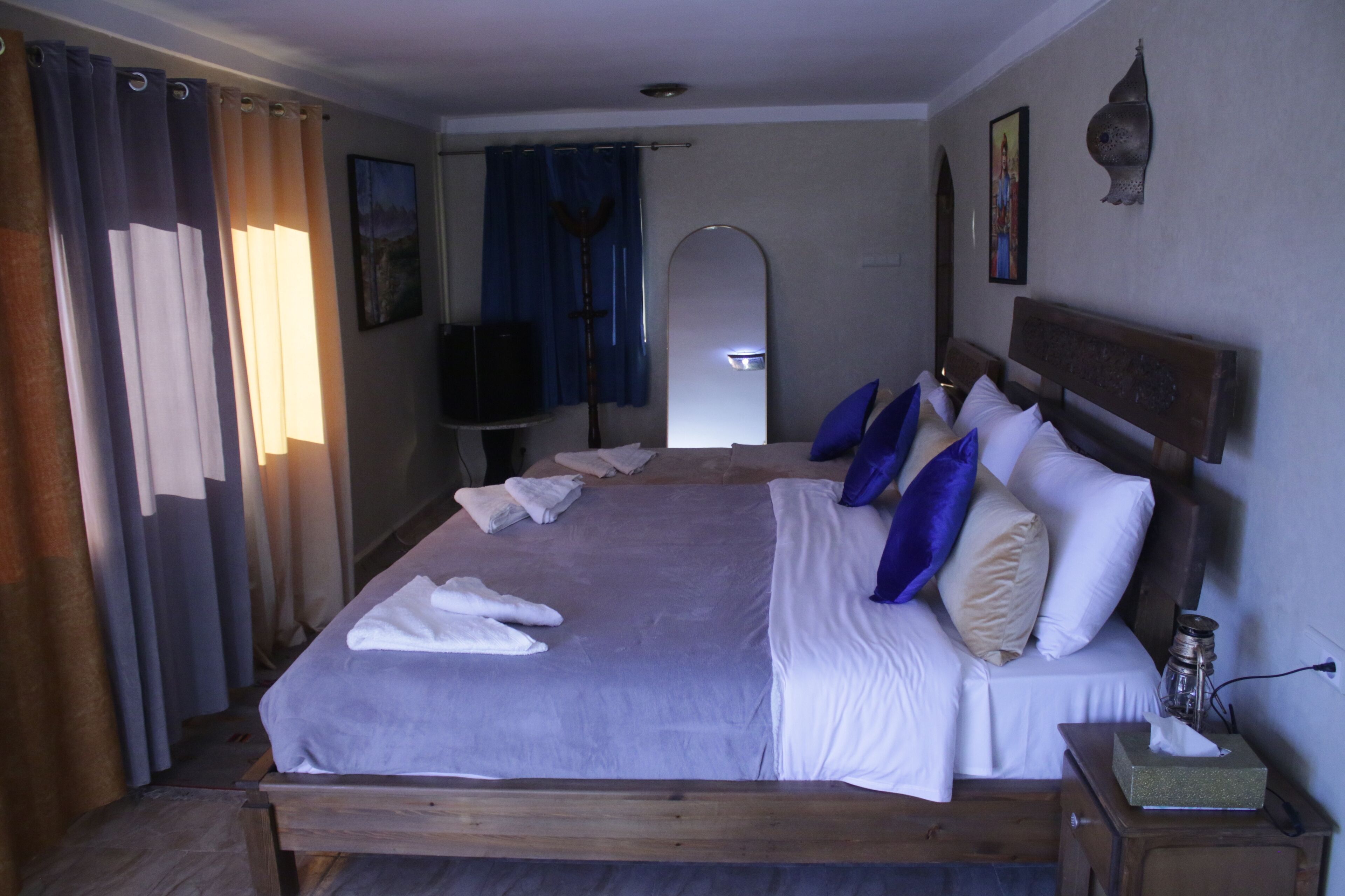 A neatly made bed with white and blue pillows, a wooden headboard, and a bedside table with a tissue box.