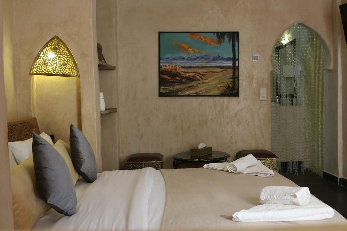 Een hotelkamer met een bed, kussens, een schilderij, een tafeltje en een spiegel.
