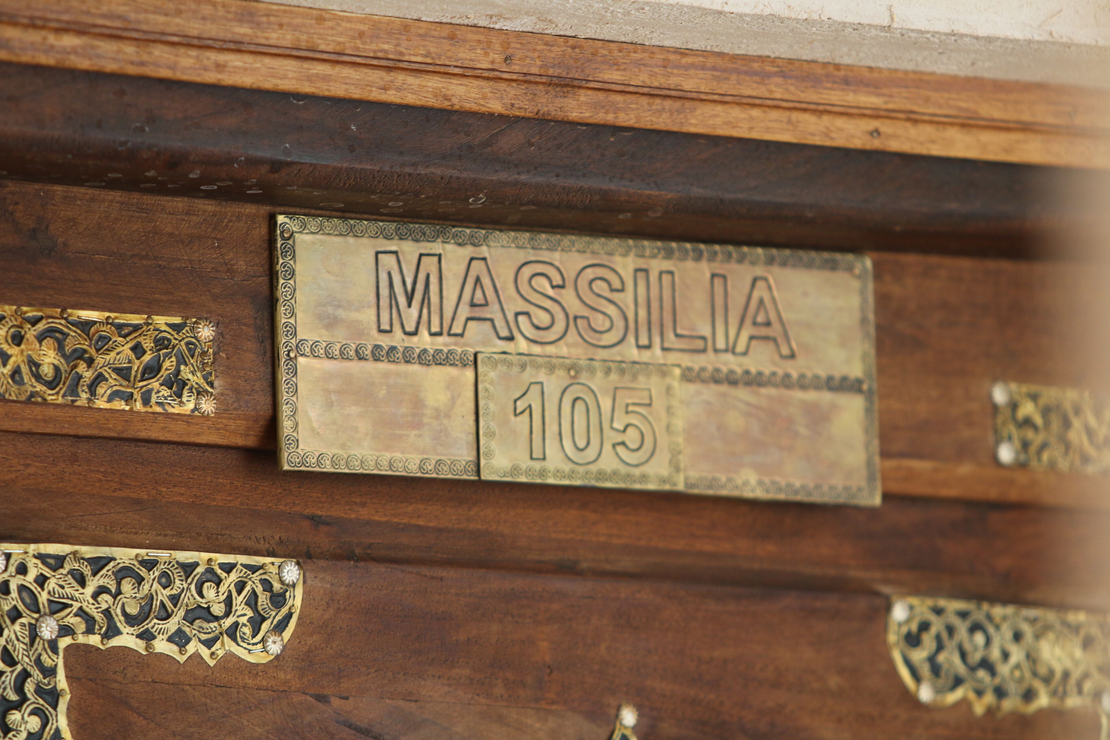 A wooden door with a brass plaque reading "MASSILIA 105".