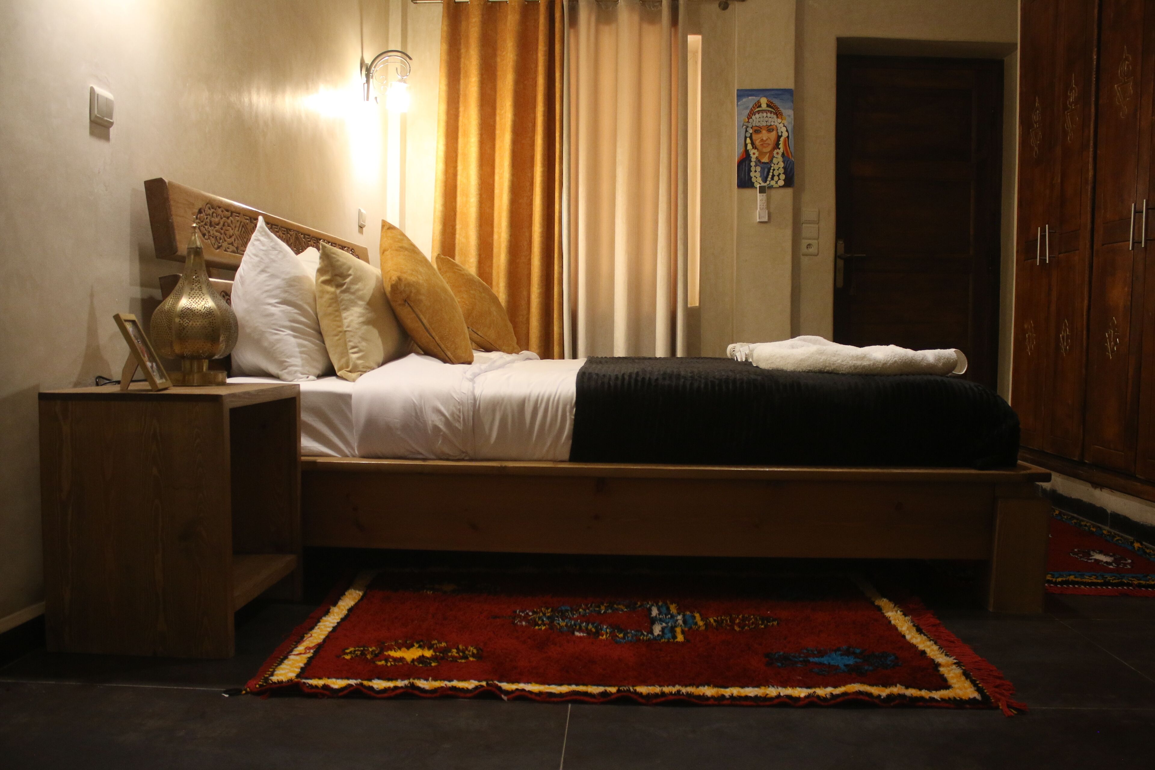 A neatly made bed with a headboard, a bedside table with a lamp, and a colorful rug on the floor.