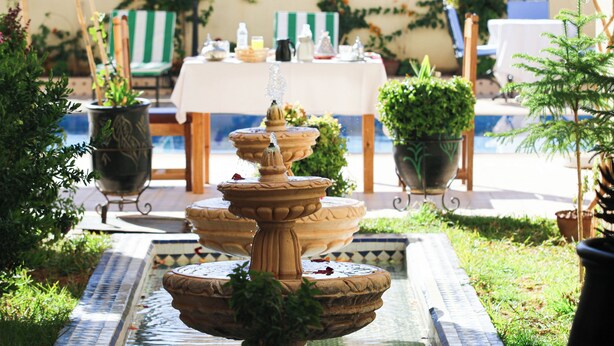 Une fontaine en pierre à plusieurs niveaux, avec une table et des chaises en arrière-plan.