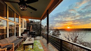 A wooden deck with a table and chairs, overlooking a body of water during sunset. - Dream Balcony Lakehouse ~Golf Cart ~Games ~Kayaks (Temple)