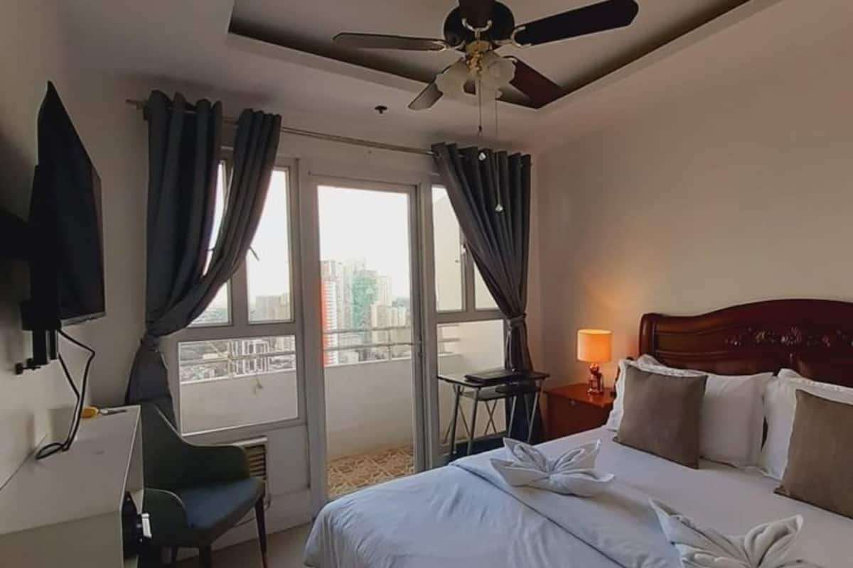 A hotel room with a bed, a desk, a chair, a ceiling fan, and a window with curtains.