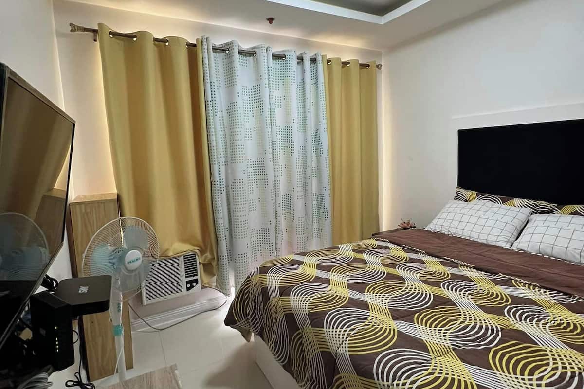 A bedroom with a bed, curtains, a ceiling fan, and a desk with a computer.