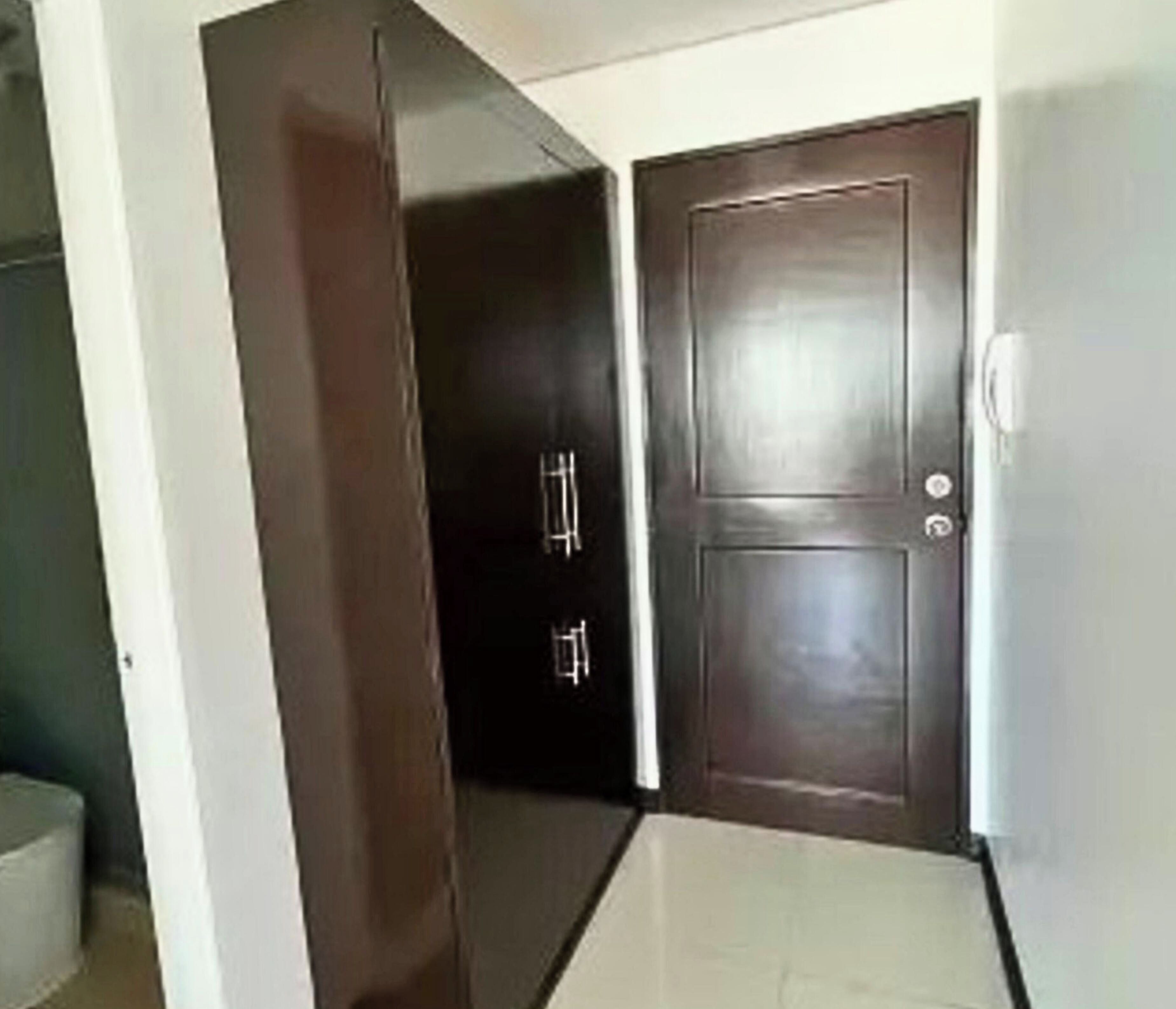 A hallway with a wooden door, a white wall, and a tiled floor.