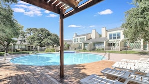 A swimming pool with lounge chairs, wooden deck, and houses in the background.