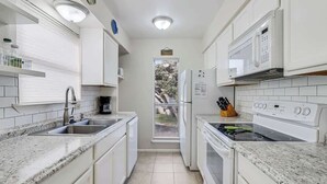 A compact kitchen with white cabinets, a built-in microwave, a stove, and a sink.